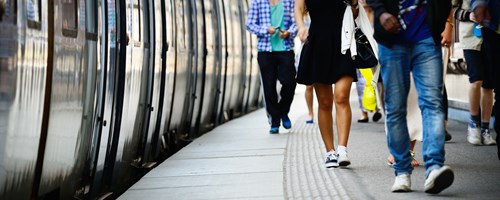 People walking on station platform with train pulled up to the platform.